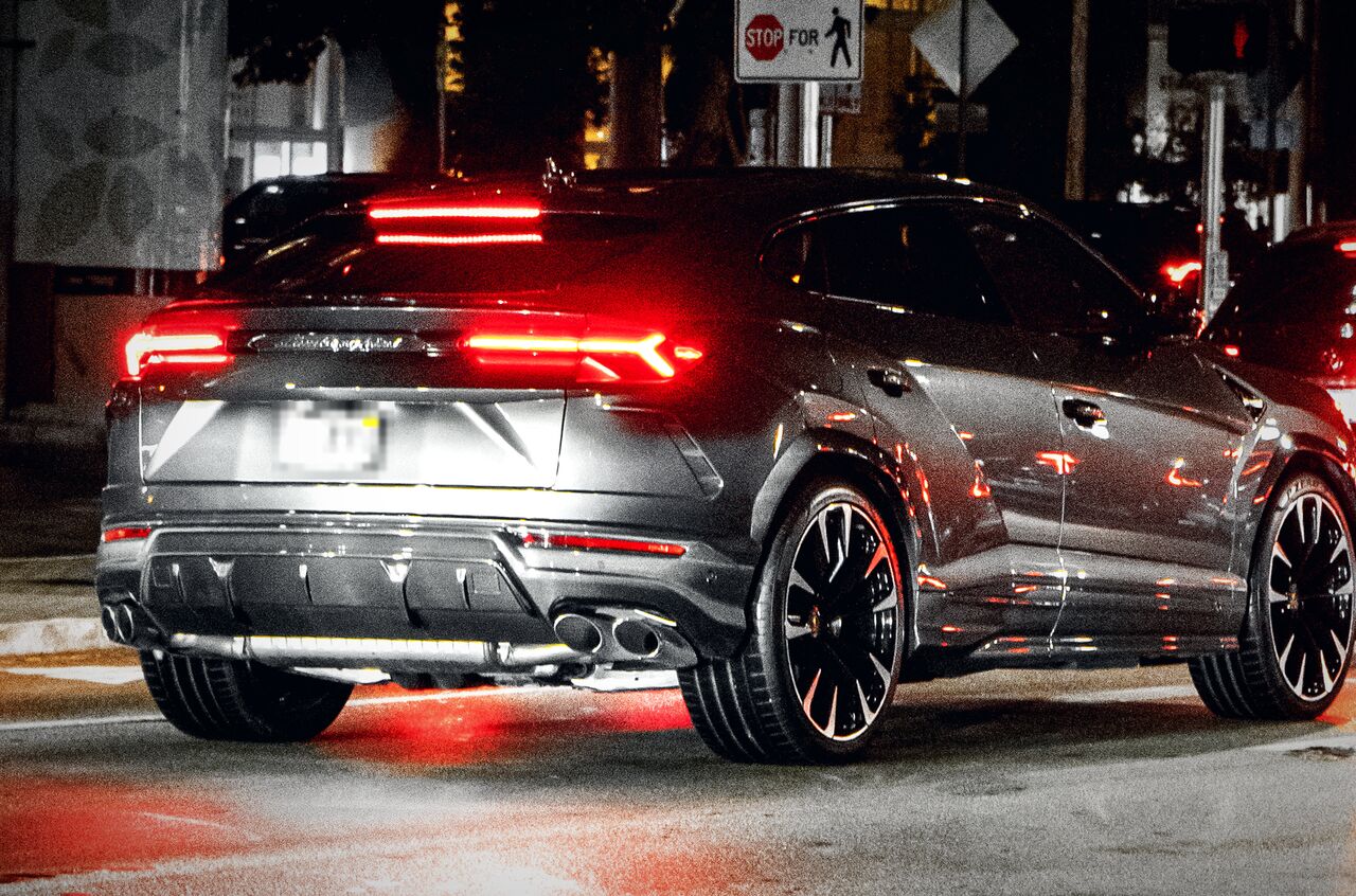 Traseira de um Lamborghini Urus cinza à noite, com as lanternas acesas e o porta-malas fechado
